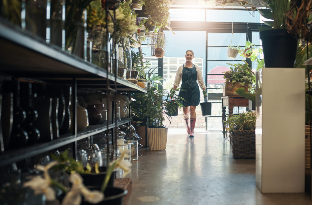 Full length shot of a young florist (business owner) carrying buckets while working inside her plant nursery