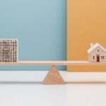 Wooden scales on a table balancing an apartment building on one side and a house on the other