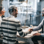 Finance broker shaking hands with young couple after successful meeting in the office. The view is through glass.