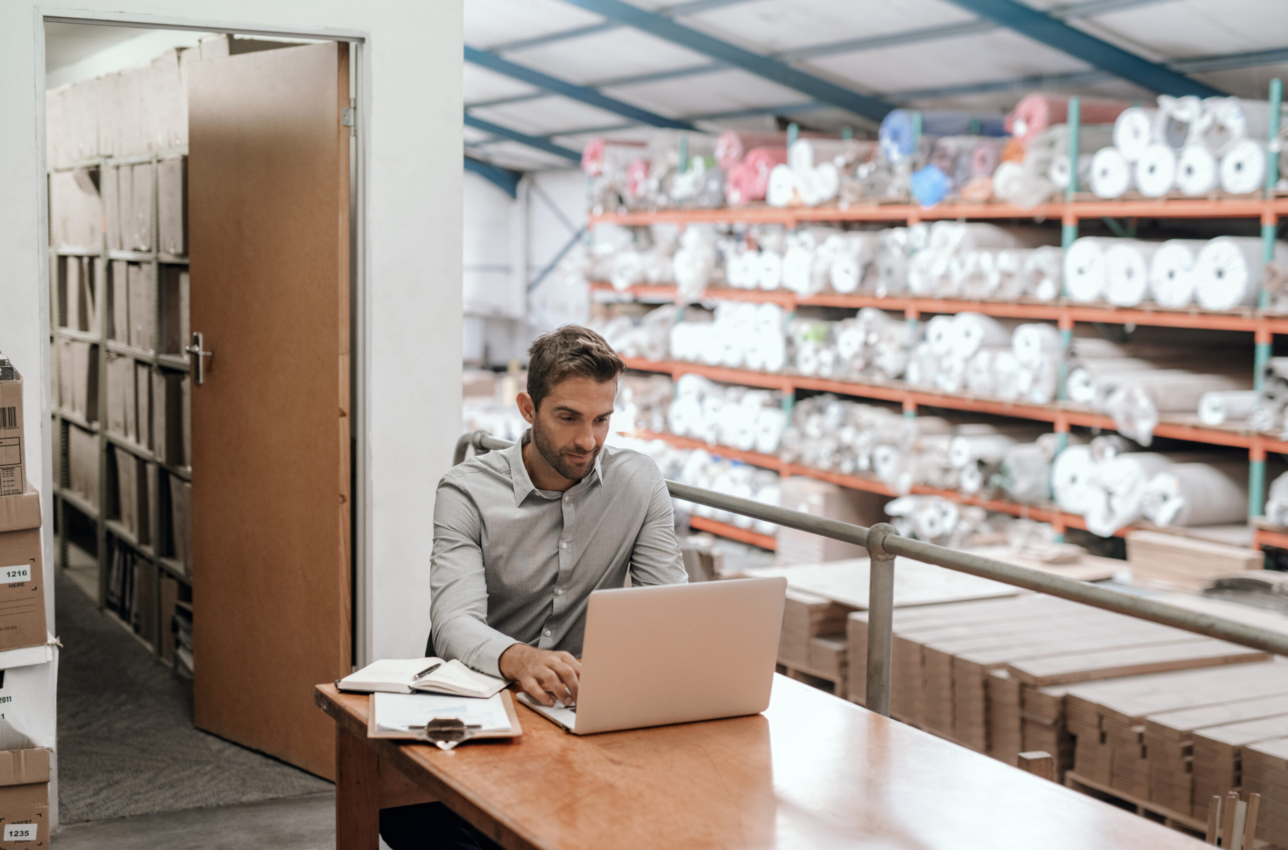 A business owner sitting at his desk working on laptop with stock shelves in the background